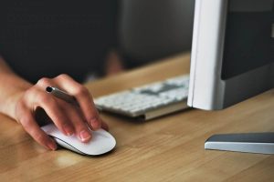 Image of hand on mouse, near keyboard and screen doing computer work